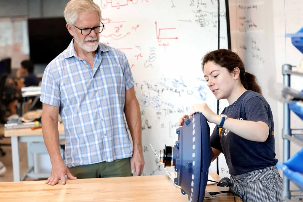 A woman holds the steering wheel, demonstrating its inflatable feedback mechanism, as a man observes.